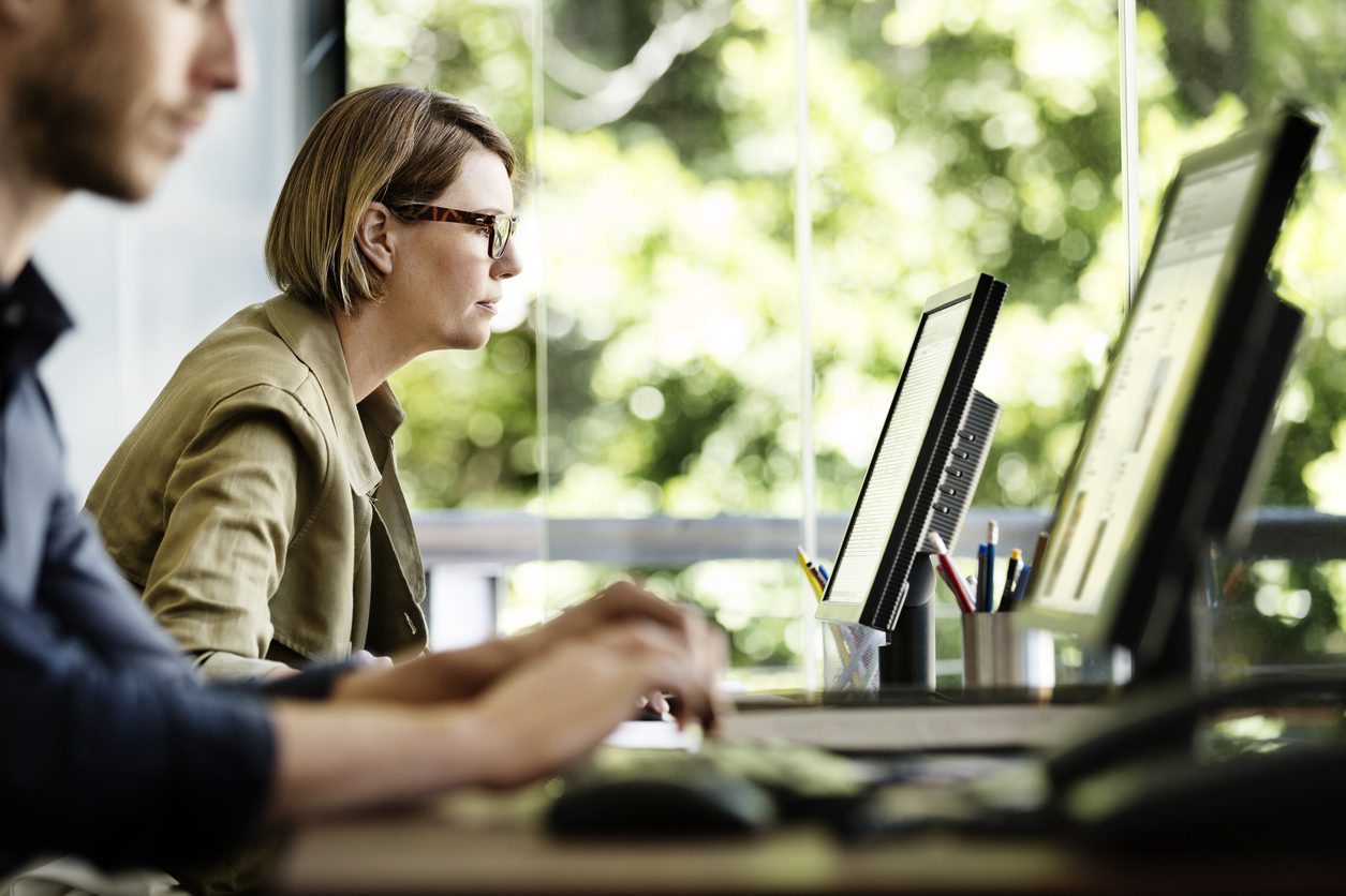 Side view of businesswoman working on computer at desk in office utilizing zero trust security 